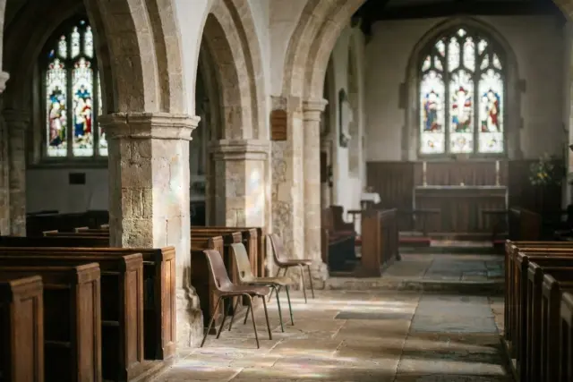 A peaceful and ancient stone church interior illuminated by soft sunlight filtering through stained glass windows